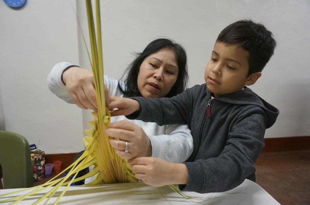Maria Consuelo Palapa weaves a palm frond in a traditional Mexican design with help from her son Omar, 7, at the Church of the Incarnation in Minneapolis on Wednesday, March 29, 2023. The parishioner at this Catholic church, where the palms will be sold as a fundraiser and blessed at Palm Sunday services this weekend, said she joined the volunteer workshop “to first help the church, and to teach the child my traditions.” (Credit: Giovanna Dell’Orto/AP.)