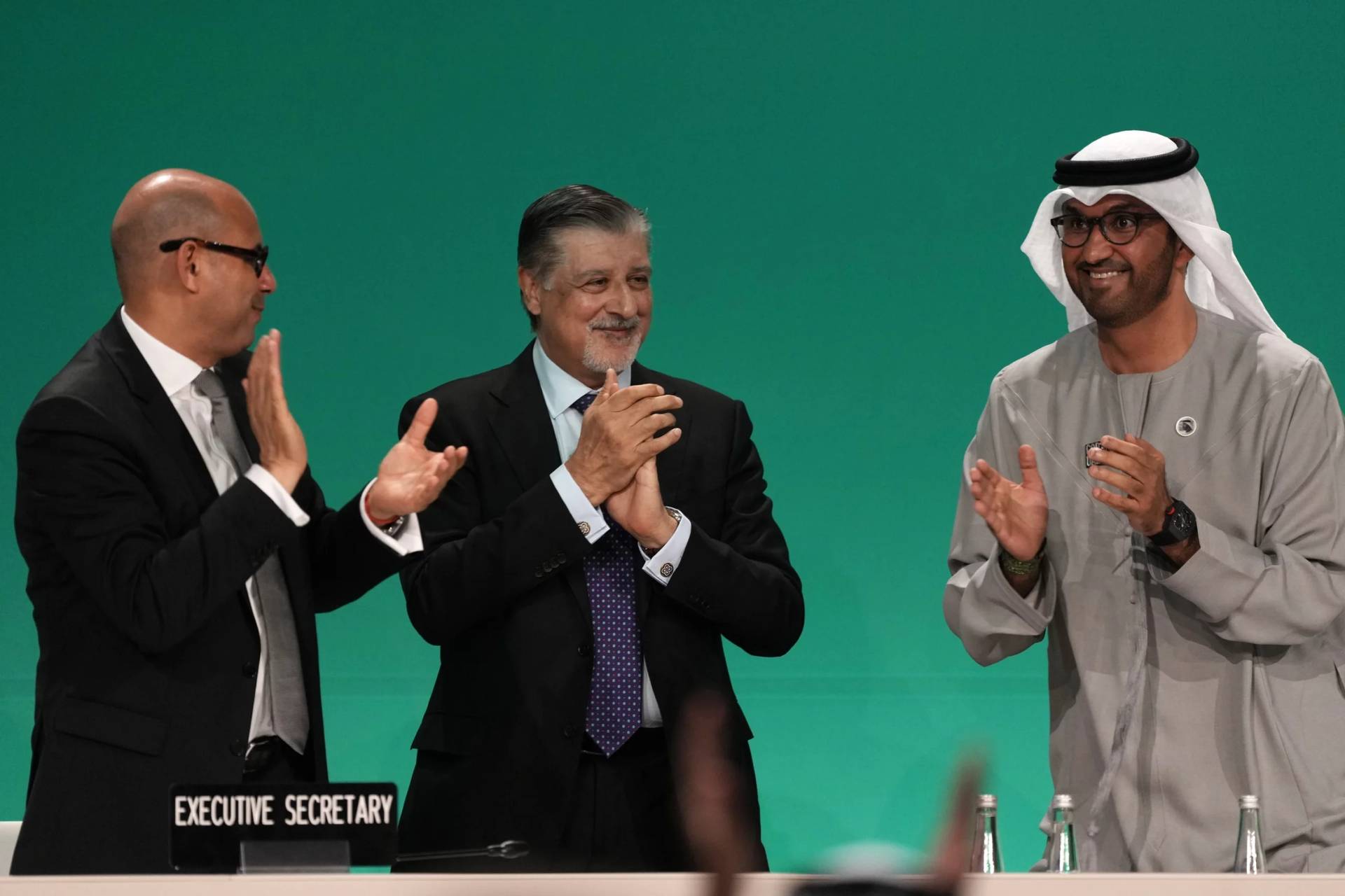 COP28 President Sultan al-Jaber, right, celebrates passing the global stocktake with United Nations Climate Chief Simon Stiell, left, and COP28 CEO Adnan Amin during a plenary session at the COP28 U.N. Climate Summit, Wednesday, Dec. 13, 2023, in Dubai, United Arab Emirates. (Credit: Kamran Jebreili/AP.)