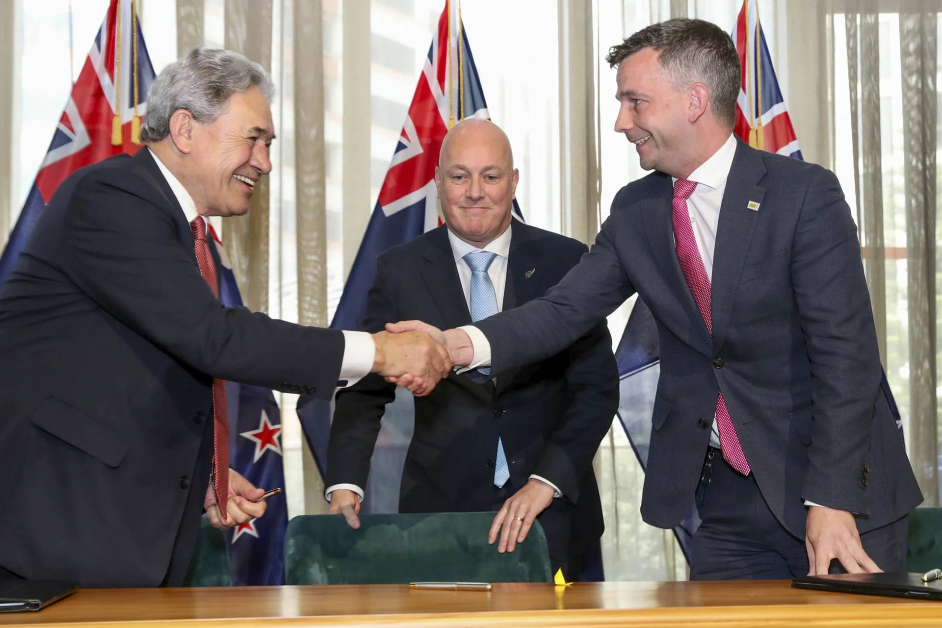 New Zealand Prime Minister elect Christopher Luxon, center, watches as his coalition partners, New Zealand First leader Winston Peters, left, and ACT leader David Seymour shake hands following a signing ceremony in Wellington, New Zealand, Friday, Nov. 24, 2023. The coalition deal ended nearly six weeks of intense negotiations after New Zealand held a general election on Oct. 14. (Credit: Mark Mitchell/NZ Herald via AP.)
