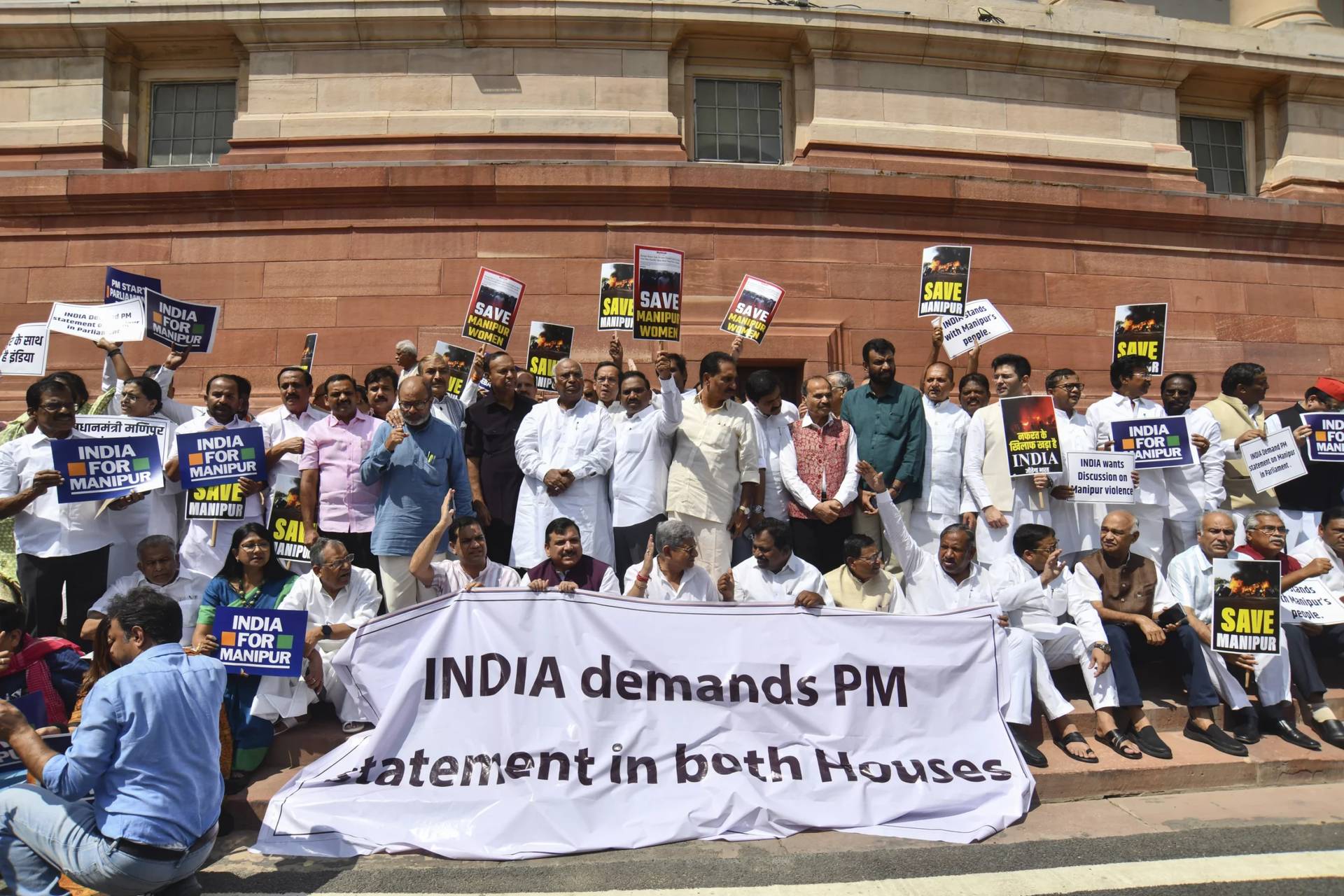 Opposition lawmakers demanding a statement from Prime Minister Narendra Modi on the violence in Manipur state carry placards and a banner with name of “INDIA” outside the Parliament building in New Delhi, India, July 24, 2023. (Credit: Altaf Qadri/AP.)