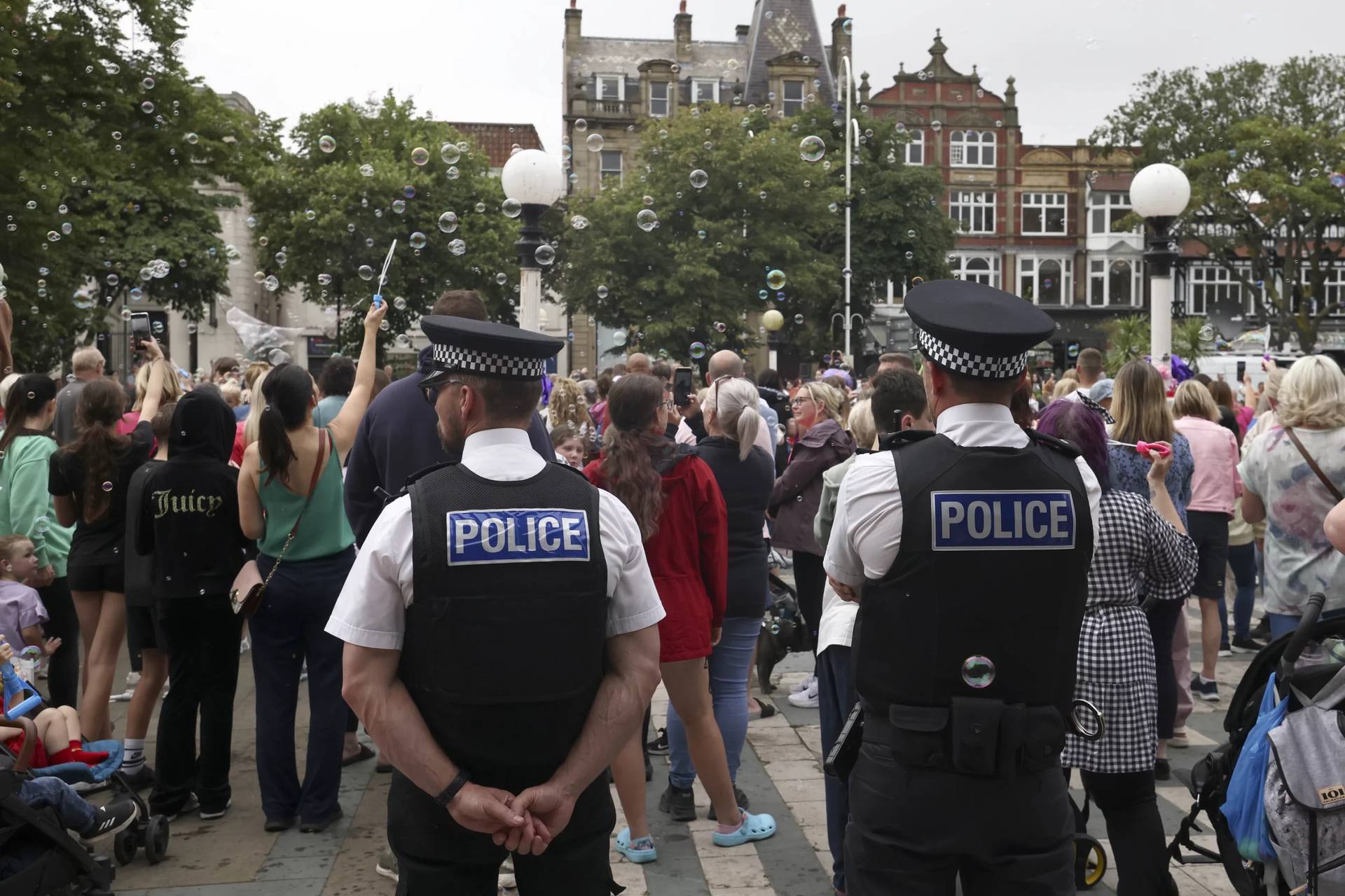 Police officers watch members of the public outside the Town Hall during a vigil for the victims of a stabbing attack in Southport, England, that happened on July 29. The vigil took place on Aug. 5. (Credit: Darren Staples/AP.)