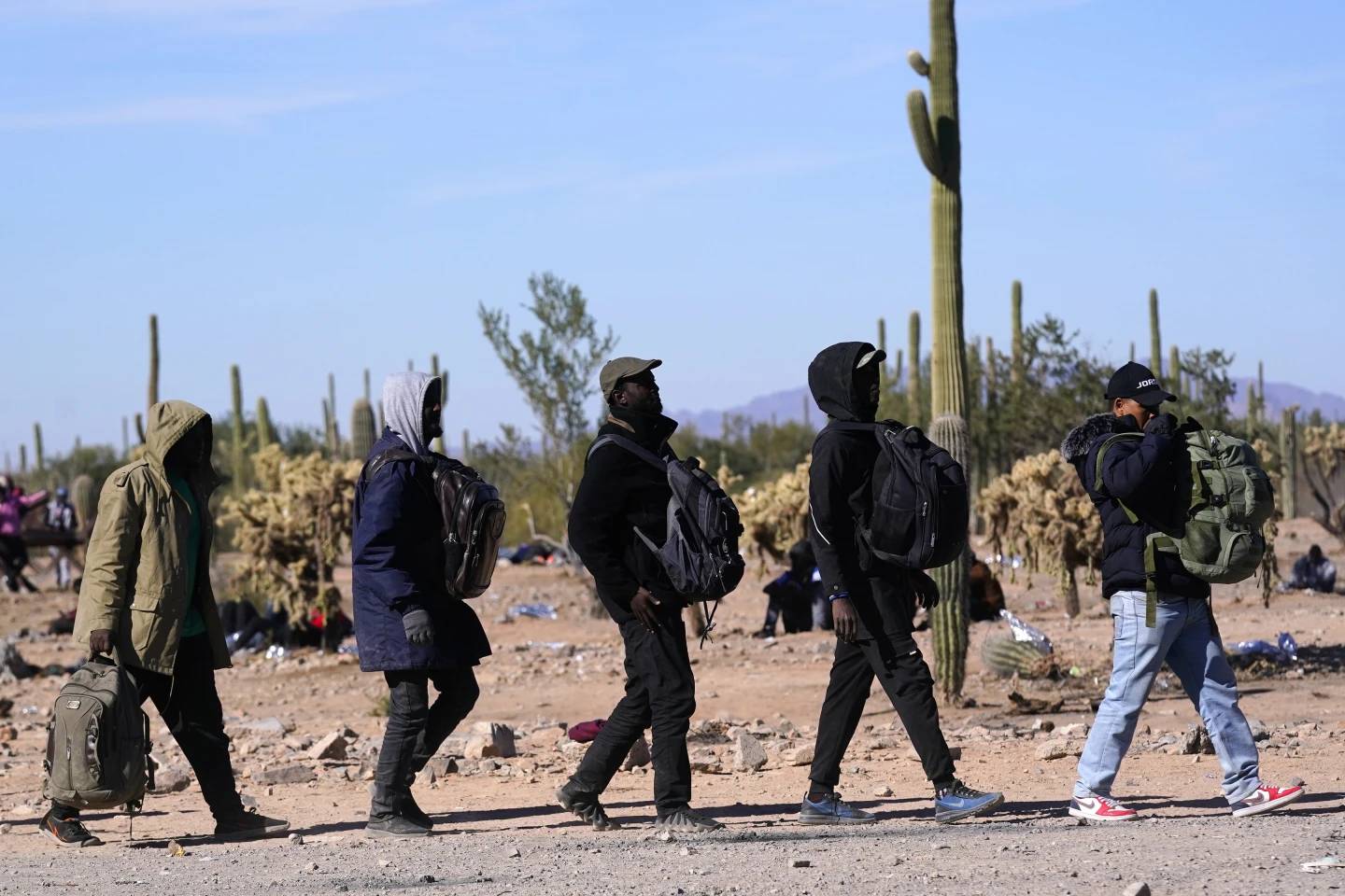 A group of migrants walk to a van as hundreds of migrants gather along the border Tuesday, Dec. 5, 2023, in Lukeville, Ariz. (Credit: Ross Franklin/AP.)