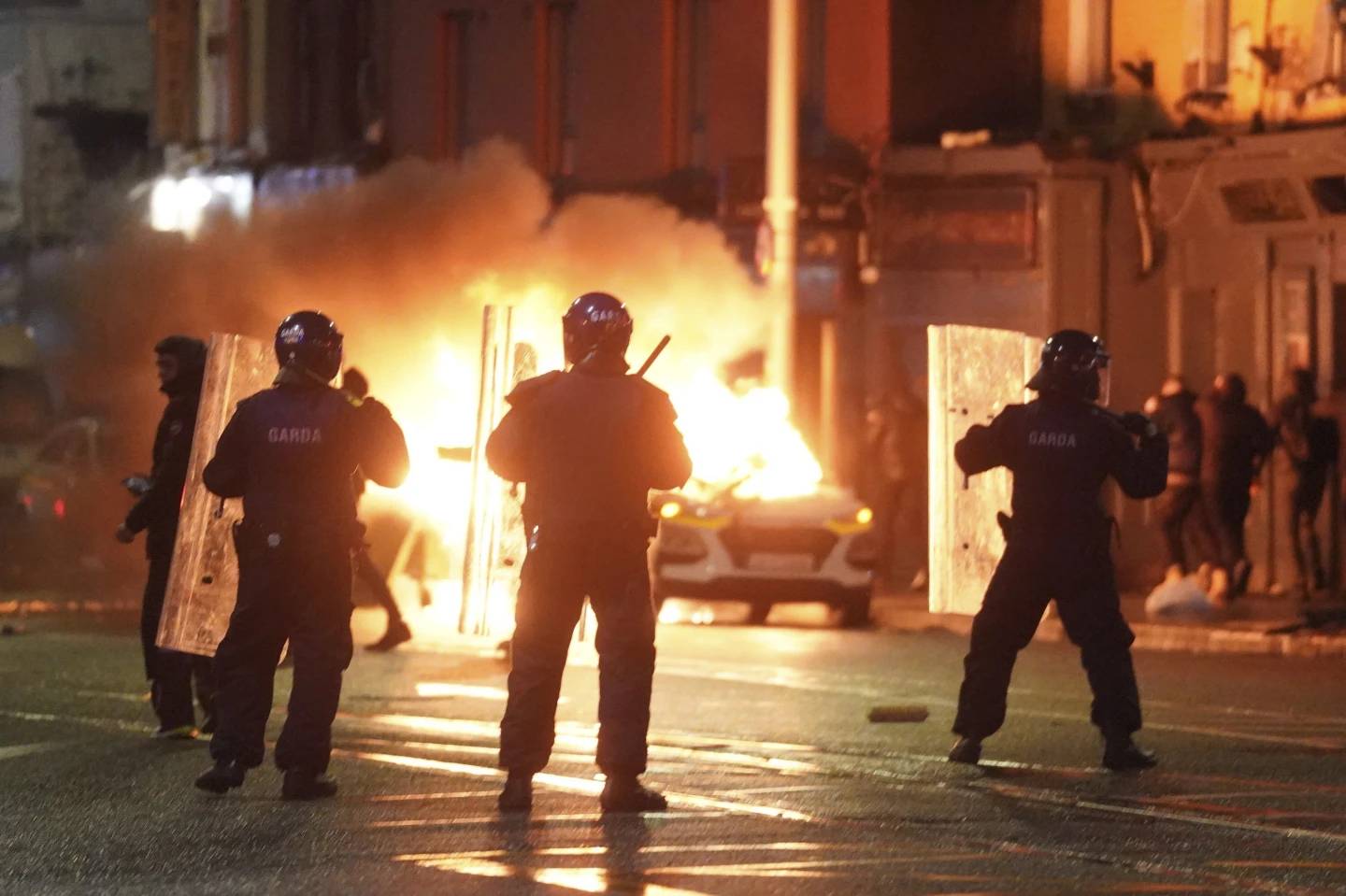 A car burns as Irish policemen stand at the scene of an attack in Dublin city center, Nov. 23, 2023. (Credit: Brian Lawless/AP.)