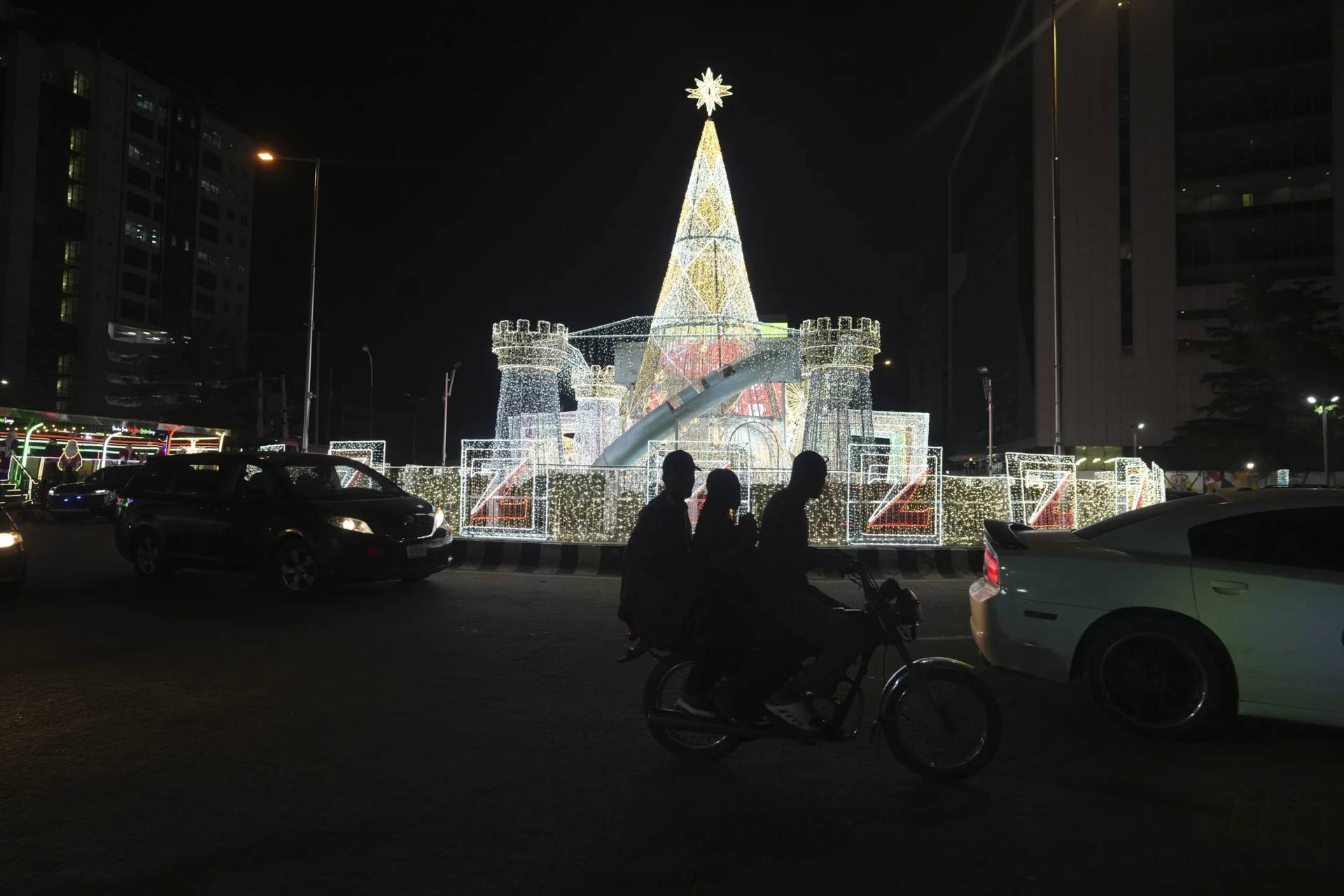 A man rides a motorcycle taxi past Christmas decorations on a street in Lago, Nigeria, on Dec. 20, 2024. (Credit: Sunday Alamba/AP.)