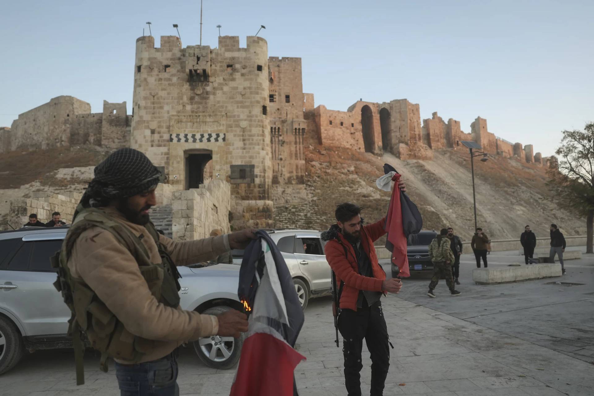 Syrian opposition fighters burn government Syrian flags for the cameras next to Aleppo’s old city, Saturday Nov. 30, 2024. (Credit: Ghaith Alsayed/AP.)