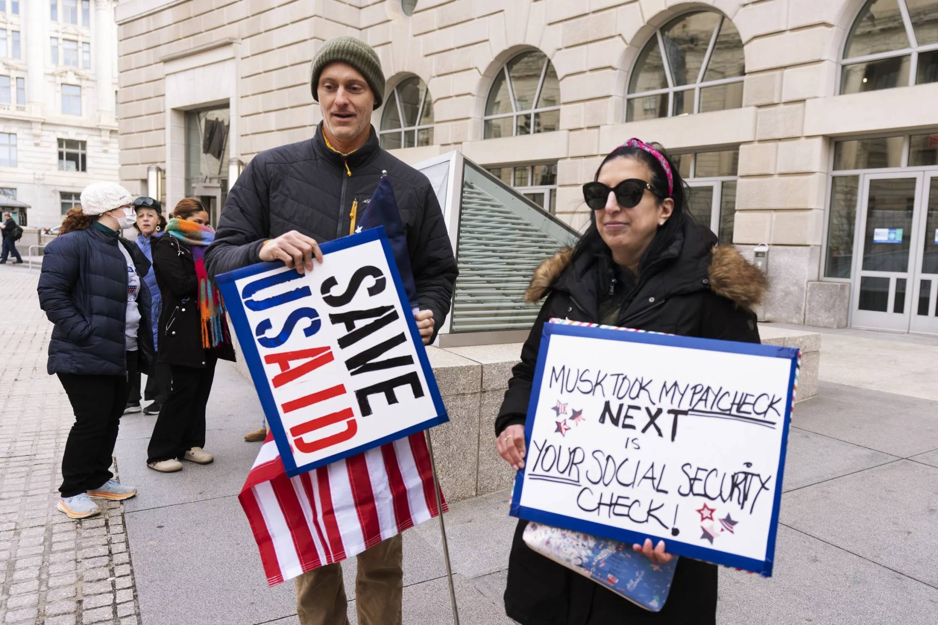 Priya Kathpal, right, and Taylor Williamson, left, who work for a company doing contract work for USAID carry signs in Washington, DC. (Credit: Manuel Balce Ceneta/AP.)