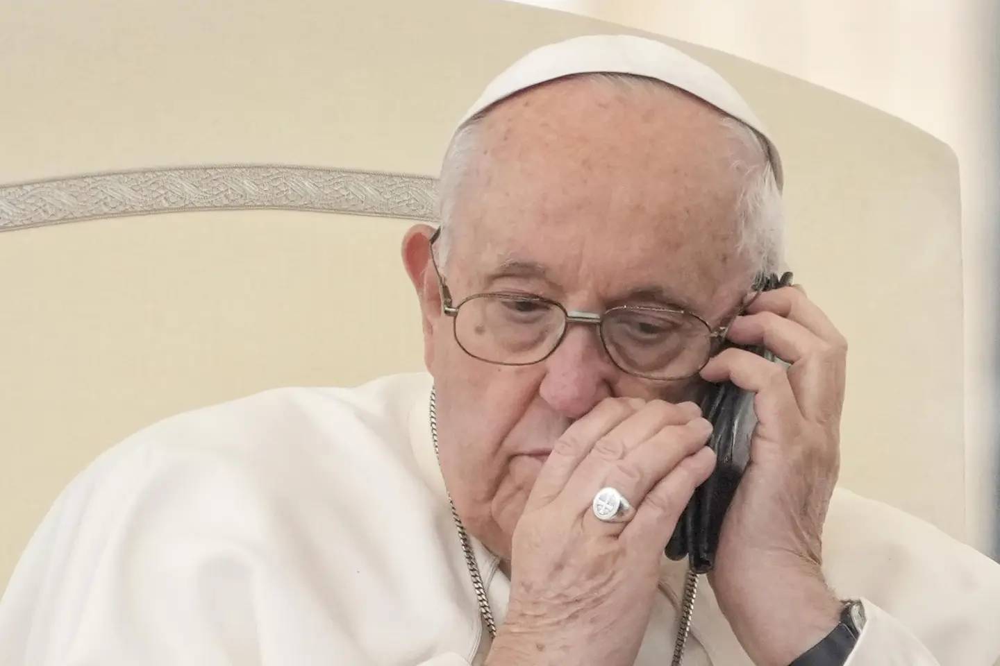 Pope Francis talks on the phone during his weekly general audience in St. Peter's Square at the Vatican on May 17, 2023. (Credit: Andrew Medichini/AP.)