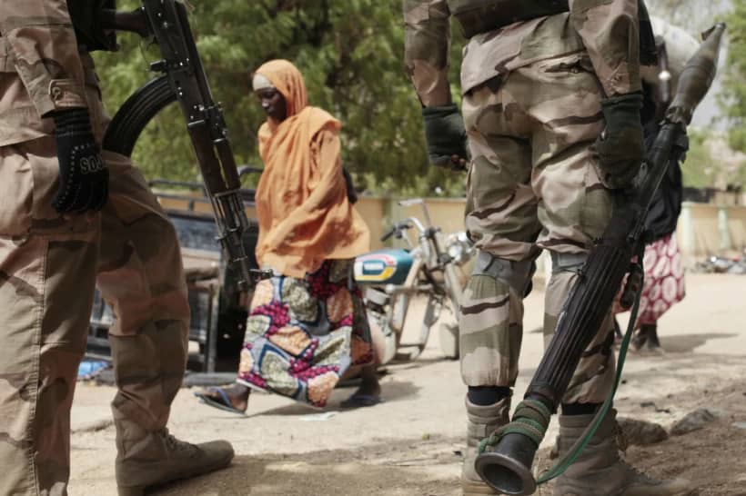 A woman walks past Nigerian soldiers at a checkpoint in Gwoza, Nigeria, a town newly liberated from Boko Haram, Wednesday April 8, 2015. (Credit: Lekan Oyekanmi/AP.)