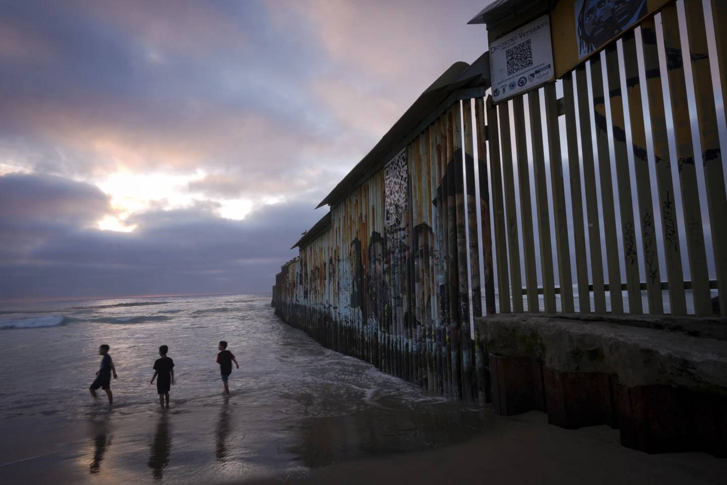 Three children play where the border wall separating Mexico and the United States meets the Pacific Ocean, Friday, Feb. 21, 2025, in Tijuana, Mexico. (Credit: Gregory Bull/AP.)