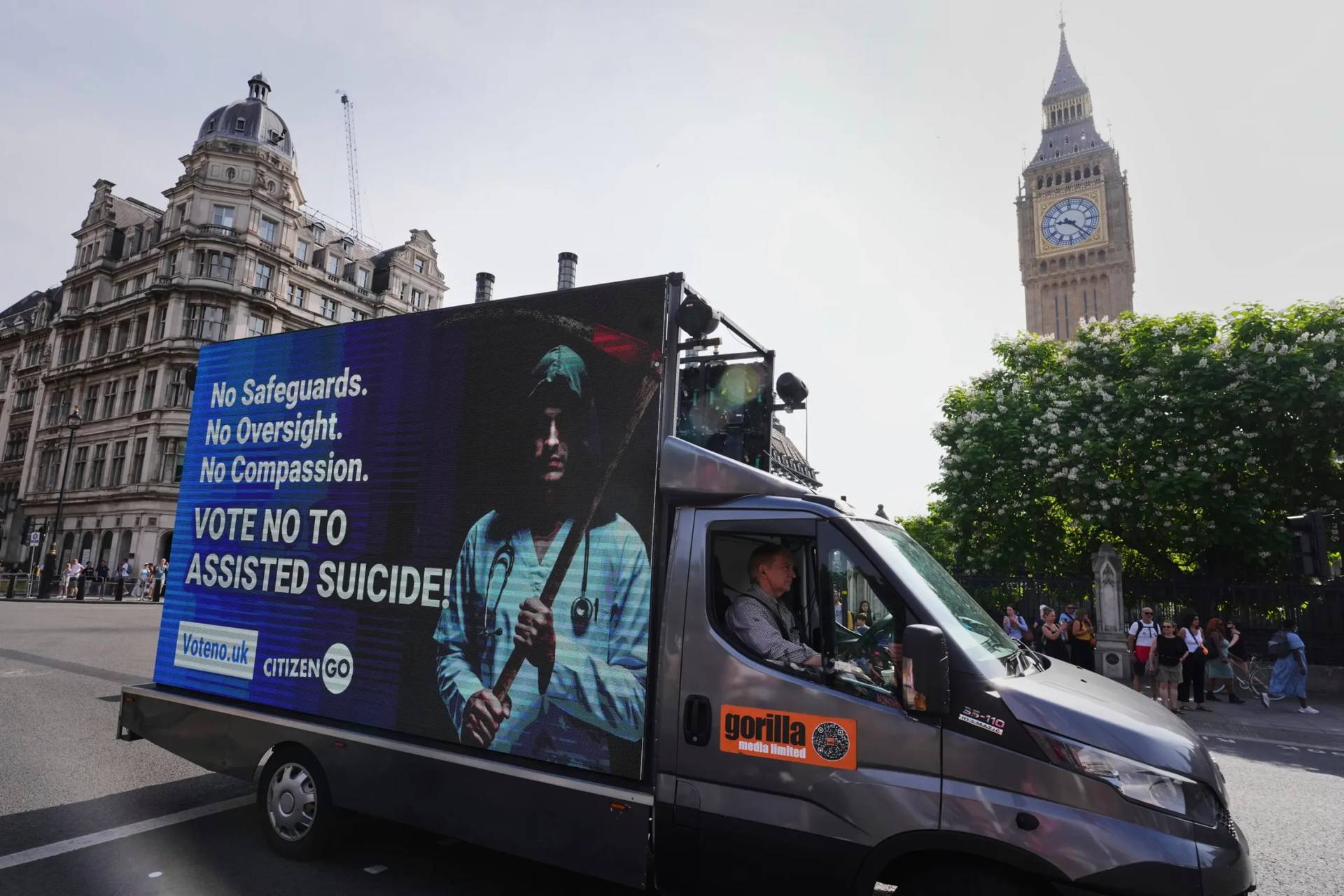 A van displaying a sign passes Big Ben as demonstrators both for and against assisted dying hold banners outside Parliament in London, Friday, June 20, 2025, as British lawmakers are set to vote Friday on whether to back a bill to help terminally ill adults end their lives in England and Wales. (Credit: Kirsty Wigglesworth/AP.)