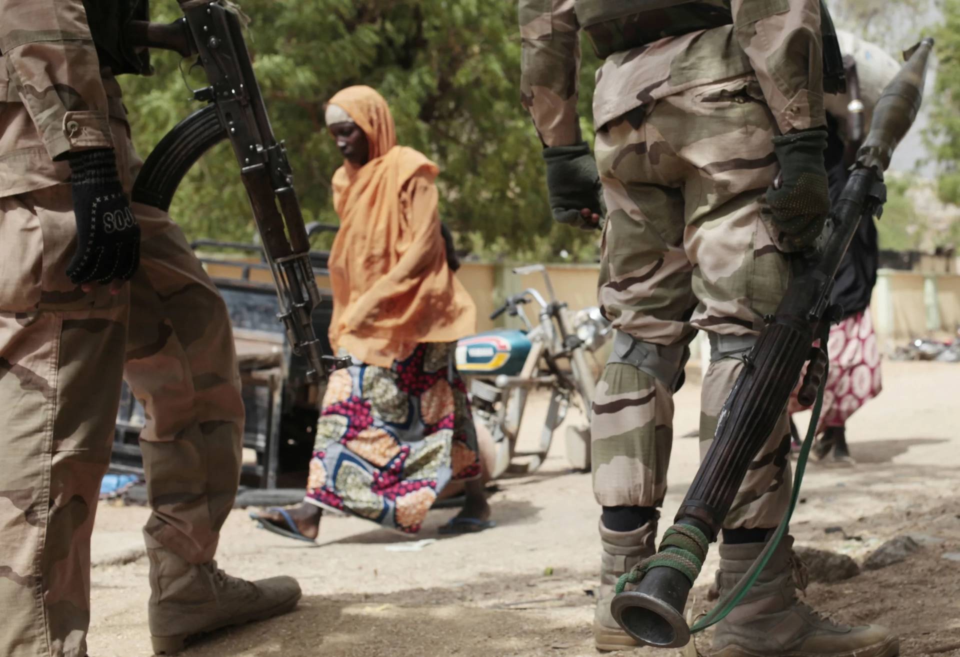 A woman walks near soldiers in Gwoza, Nigeria, on April 8, 2015. (Credit: Lecan Oyekanmi/AP.)