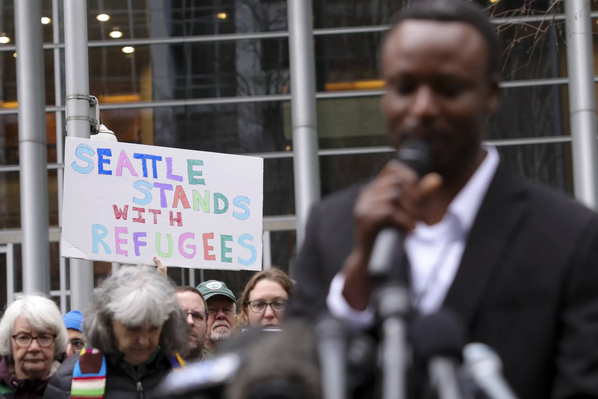Signs are seen supporting refugees as Tshishiku Henry, a former refugee and Washington Delegate for the Refugee Conference, speaks in Seattle, Washington, on Feb. 25, 2025. (Credit: Ryan Sun/AP.)