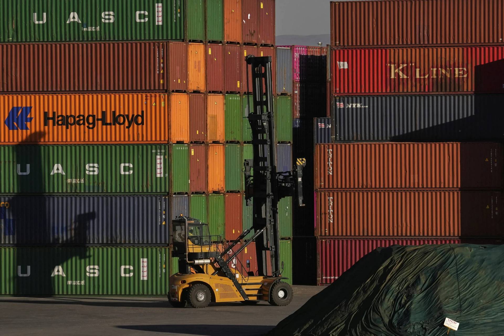 A heavy machine drives past shipping containers stacked at a depo in Johannesburg, South Africa, on Aug. 1, 2025. (Credit: Themba Hadebe/AP.)