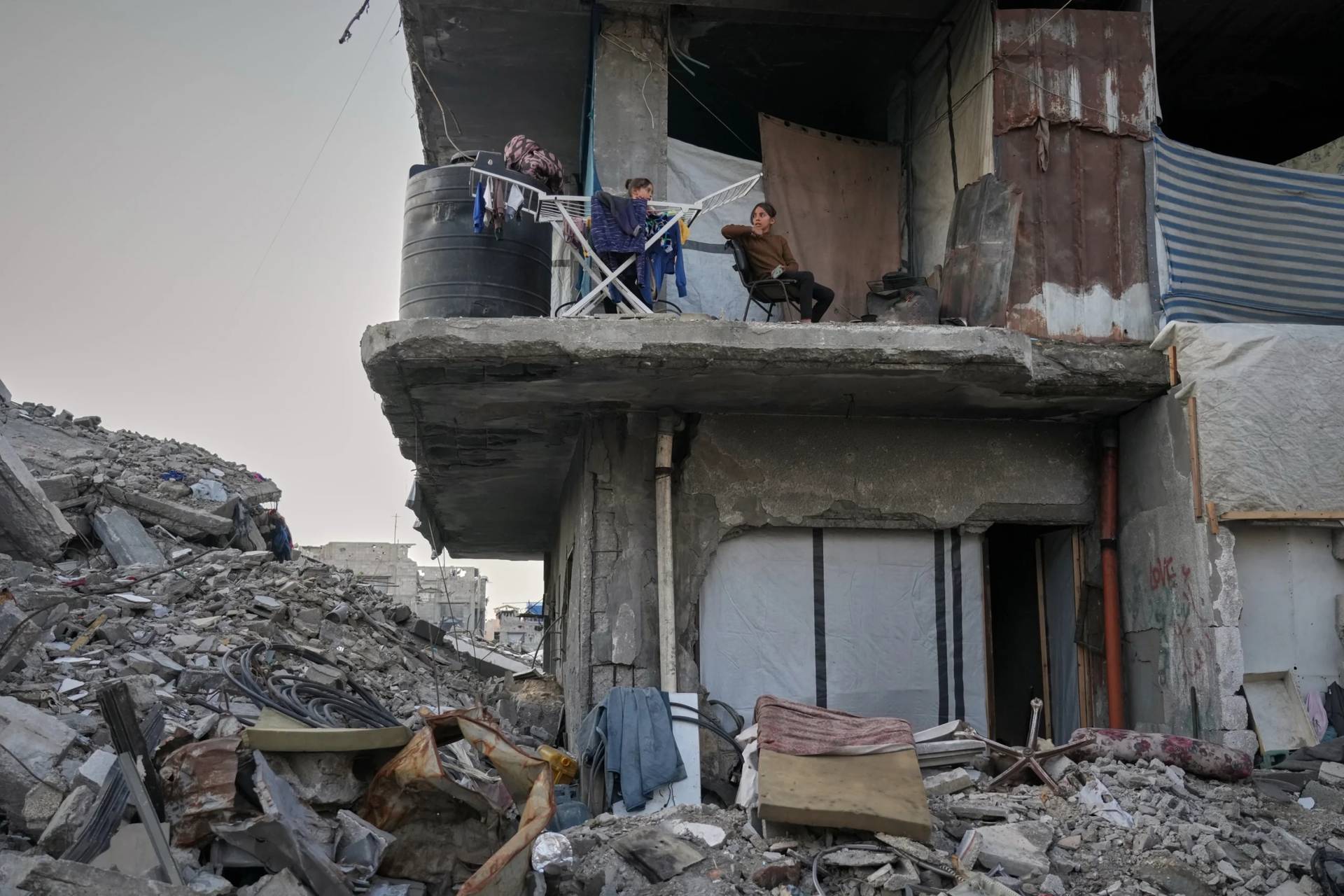 Two girls sit next to their drying laundry in a gutted apartment building in Gaza City, Tuesday, Nov. 18, 2025. (Credit: Jehad Alshrafi/AP.)