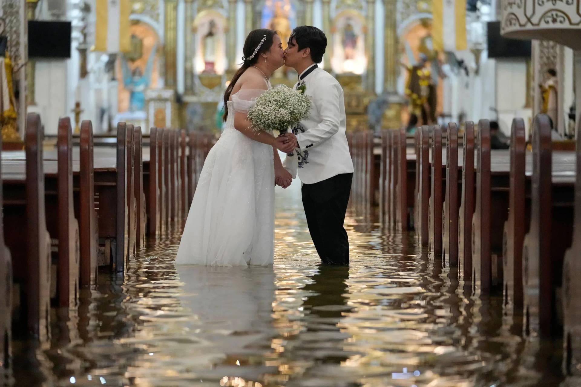 Newlyweds Jade Rick Verdillo, right, and Jamaica kiss during their wedding inside a flooded Barasoain church in Malolos, Philippines, July 22, 2025. (Credit: Aaron Favila/AP.)