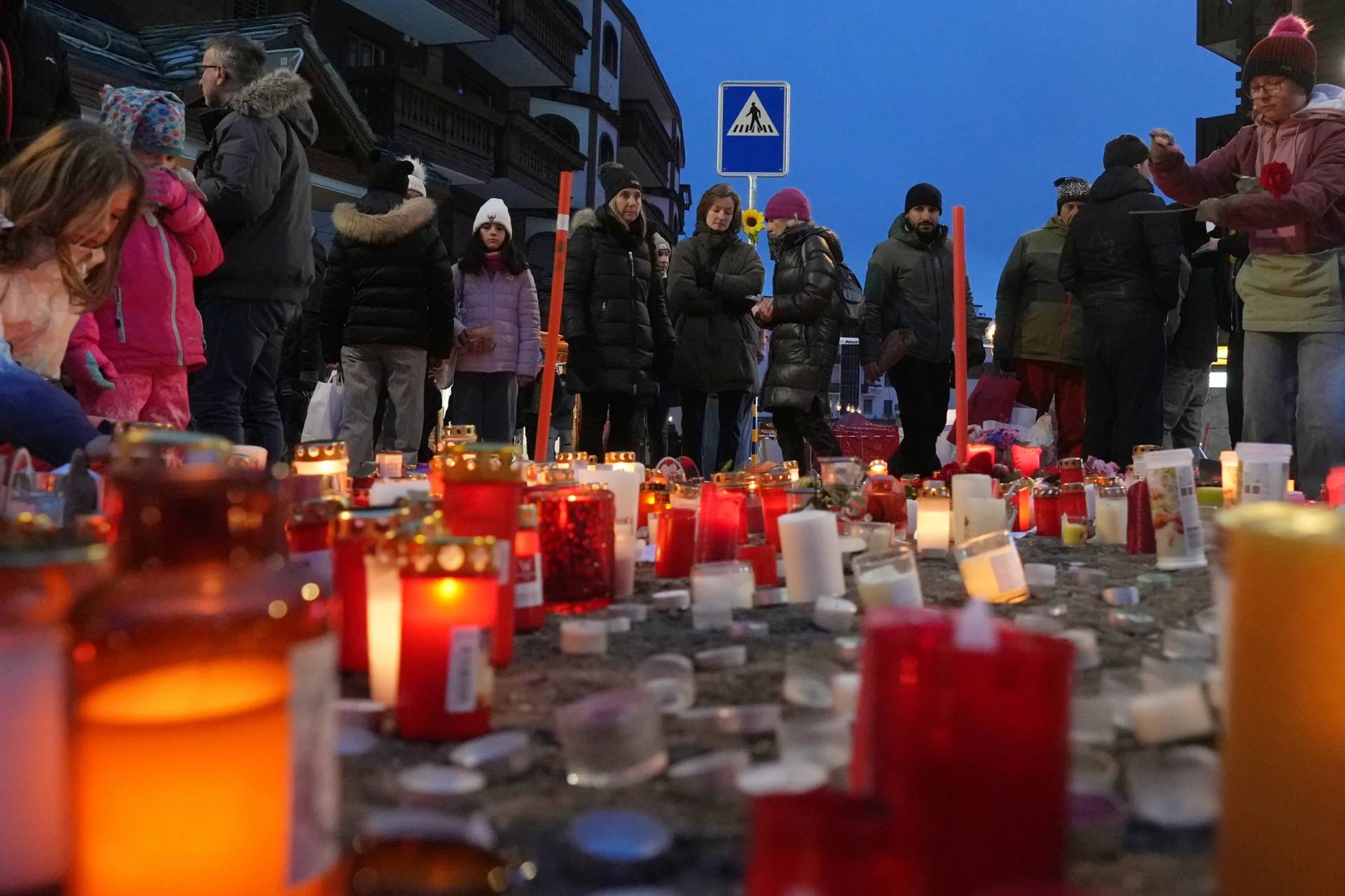 People light candles near the sealed off Le Constellation bar in Crans-Montana, Swiss Alps, Switzerland, Friday, Jan. 2, 2026, where a devastating fire left dead and injured during the New Year’s celebrations. (Credit: Antonio Calanni/AP.)