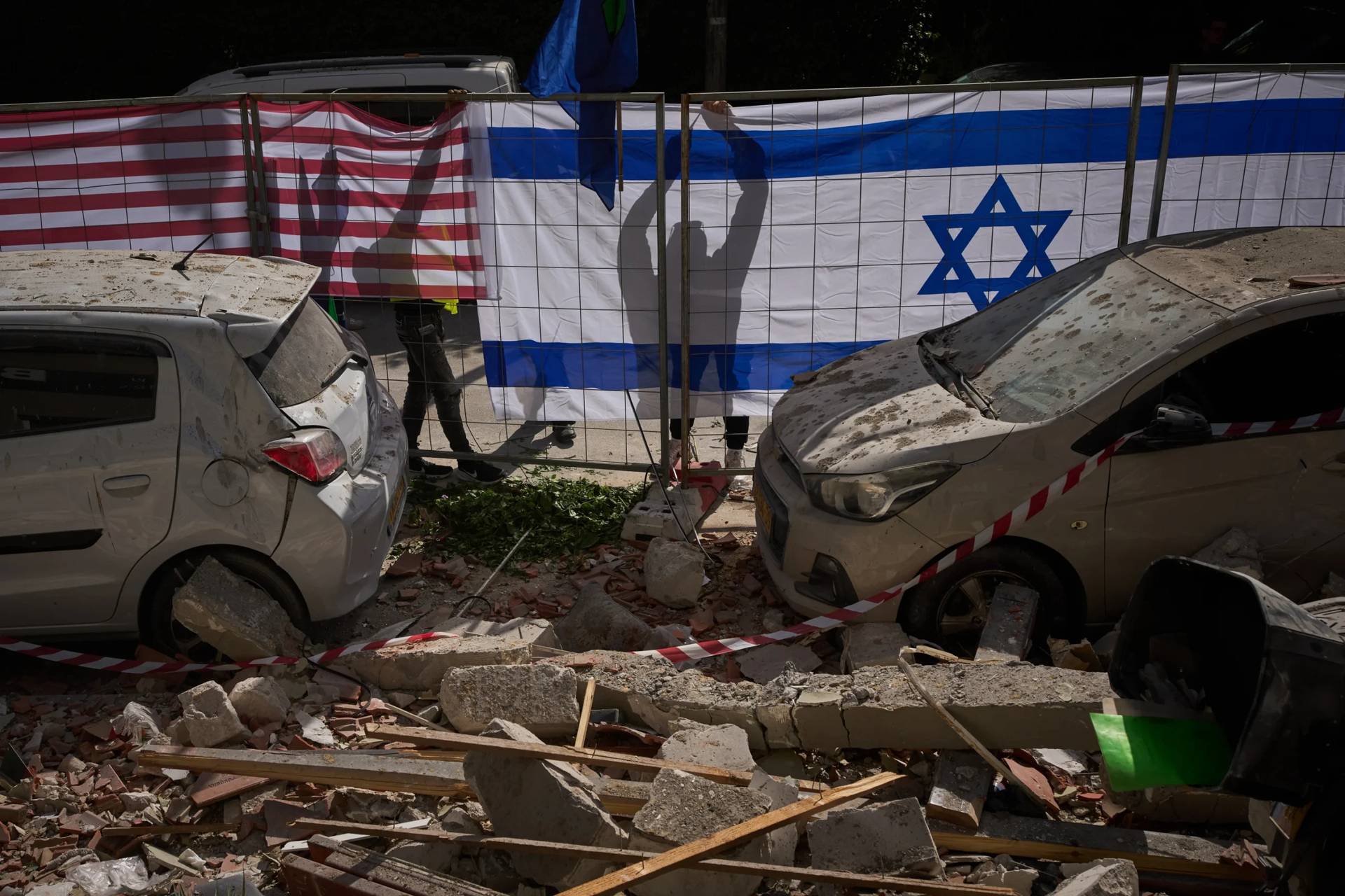 Israeli authorities hang Israeli and U.S. flags at the site struck by an Iranian missile that killed two people, in Ramat Gan, Israel, Wednesday, March 18, 2026. (Credit: Oded Balilty/AP.)