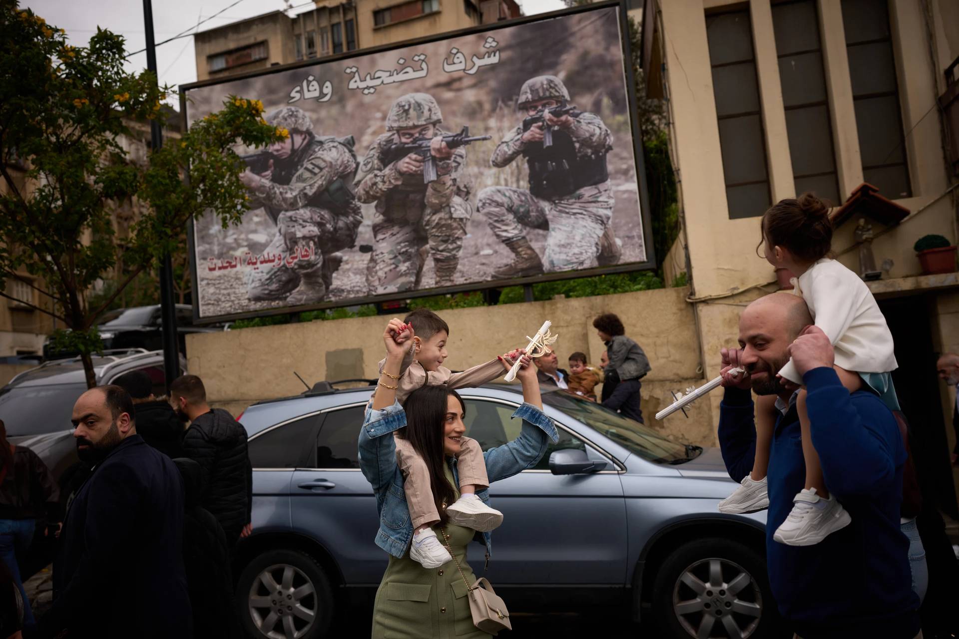 Catholic worshipers carry their children on their shoulders as they march in a procession during a Palm Sunday Mass in Beirut, Lebanon, Sunday, March 29, 2026. The poster in the background reads in Arabic: “Honor, sacrifice and loyalty”. (Credit: Emilio Morenatti/AP.)