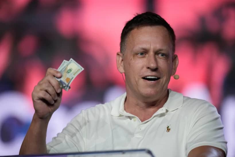 Peter Thiel, co-founder of PayPal and Palantir, offers a pair of hundred dollar bills to attendees during a keynote address at the Bitcoin Conference, April 7, 2022, in Miami Beach, Fla. (Credit: Rebecca Blackwell/AP.)