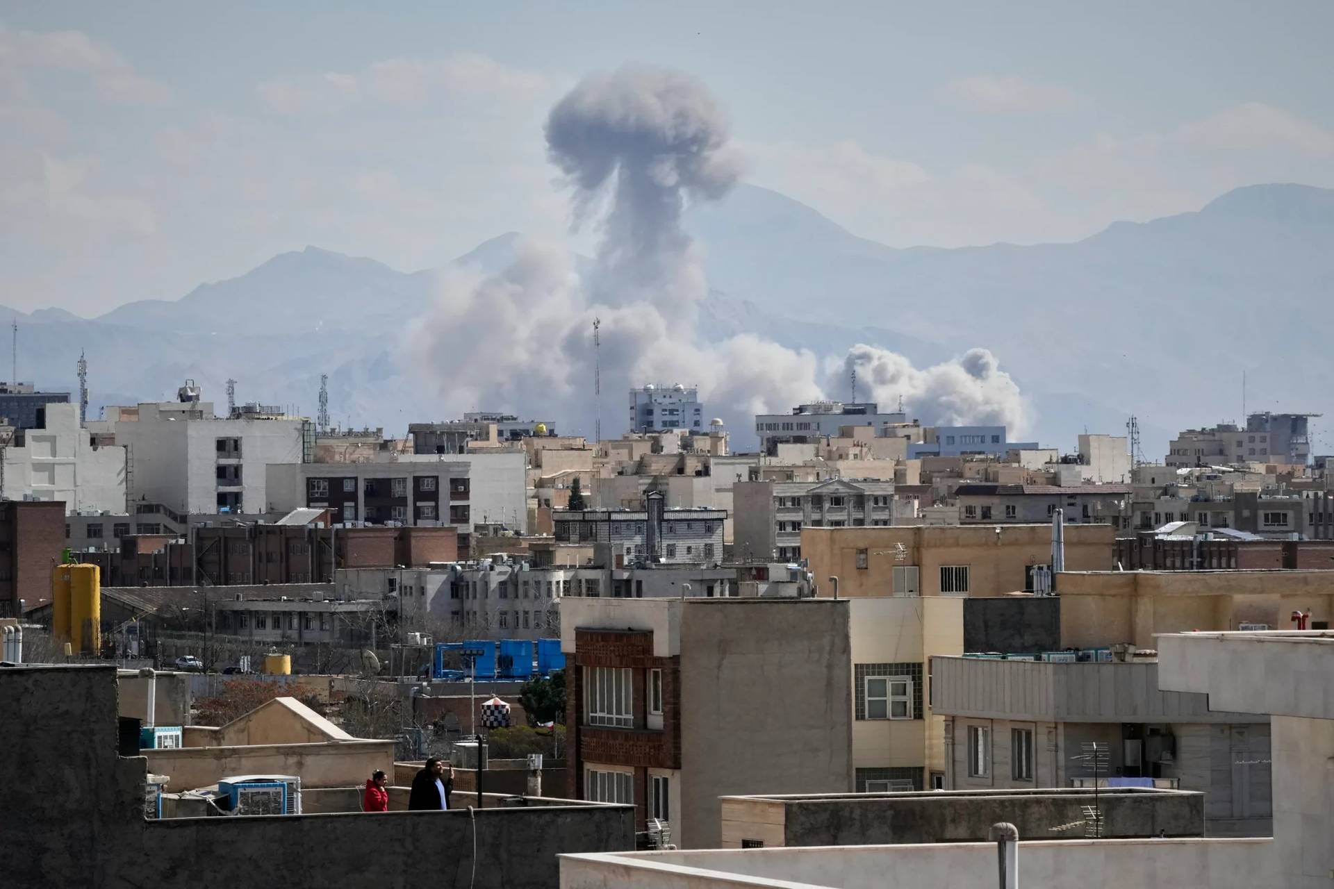 People watch from a rooftop as a plume of smoke rises after a strike in Tehran, Iran, Sunday, March 1, 2026. (Credit: Vahid Salemi/AP.)