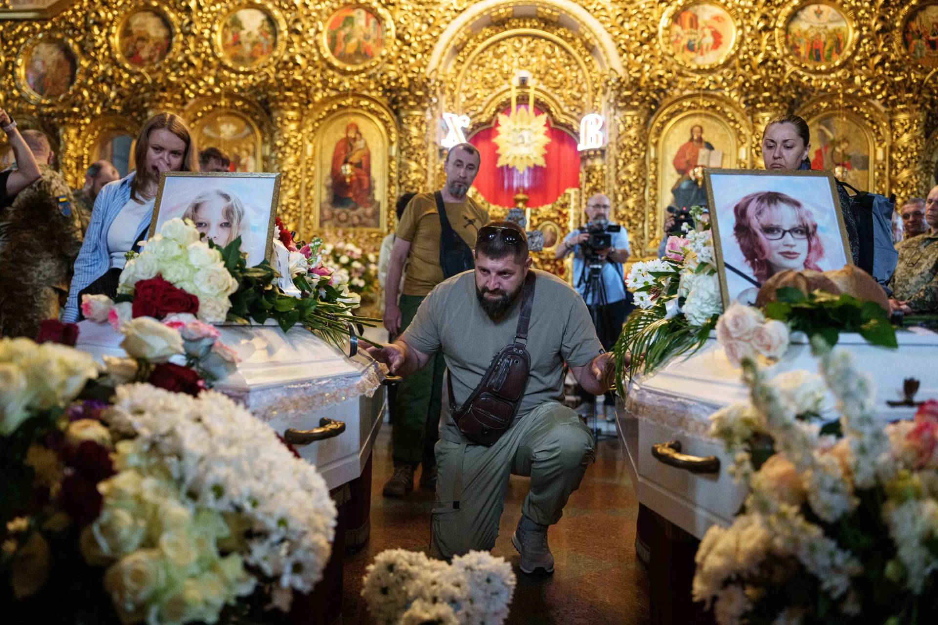 A man kneels next to the coffins of sisters Liubava and Vira Yakovleva, killed by a Russian rocket strike during their funeral in Kyiv, Ukraine, on May 19, 2026. (Credit: Evygeniy Maloletka/AP.)