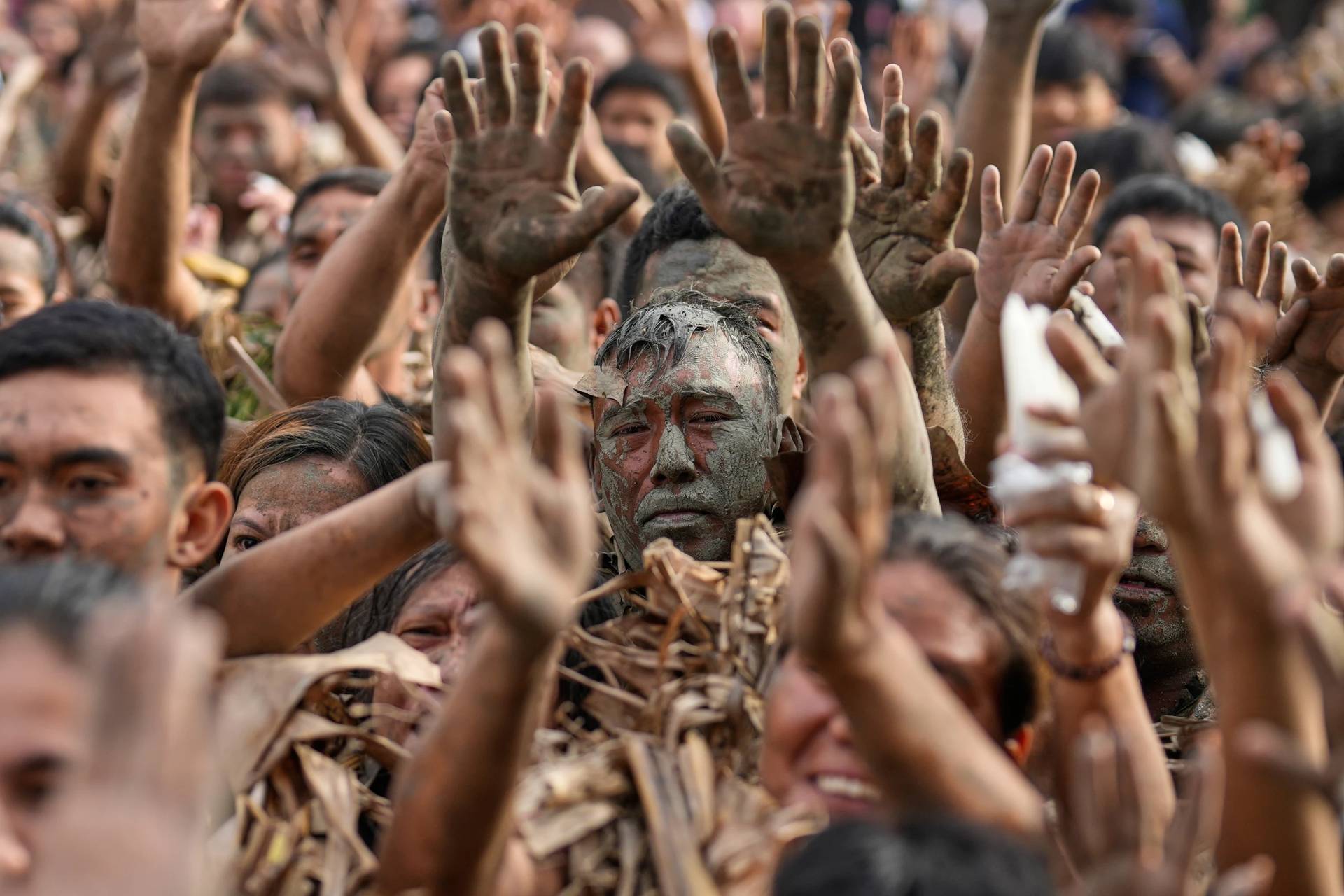 Melencio Neuda, center, and other devotees who participated in the mud people festival raise their hands during a mass on the feast day of Saint John the Baptist at Bibiclat, Nueva Ecija province, northern Philippines, Wednesday, June 24, 2026. (Credit: Aaron Favila/AP.)