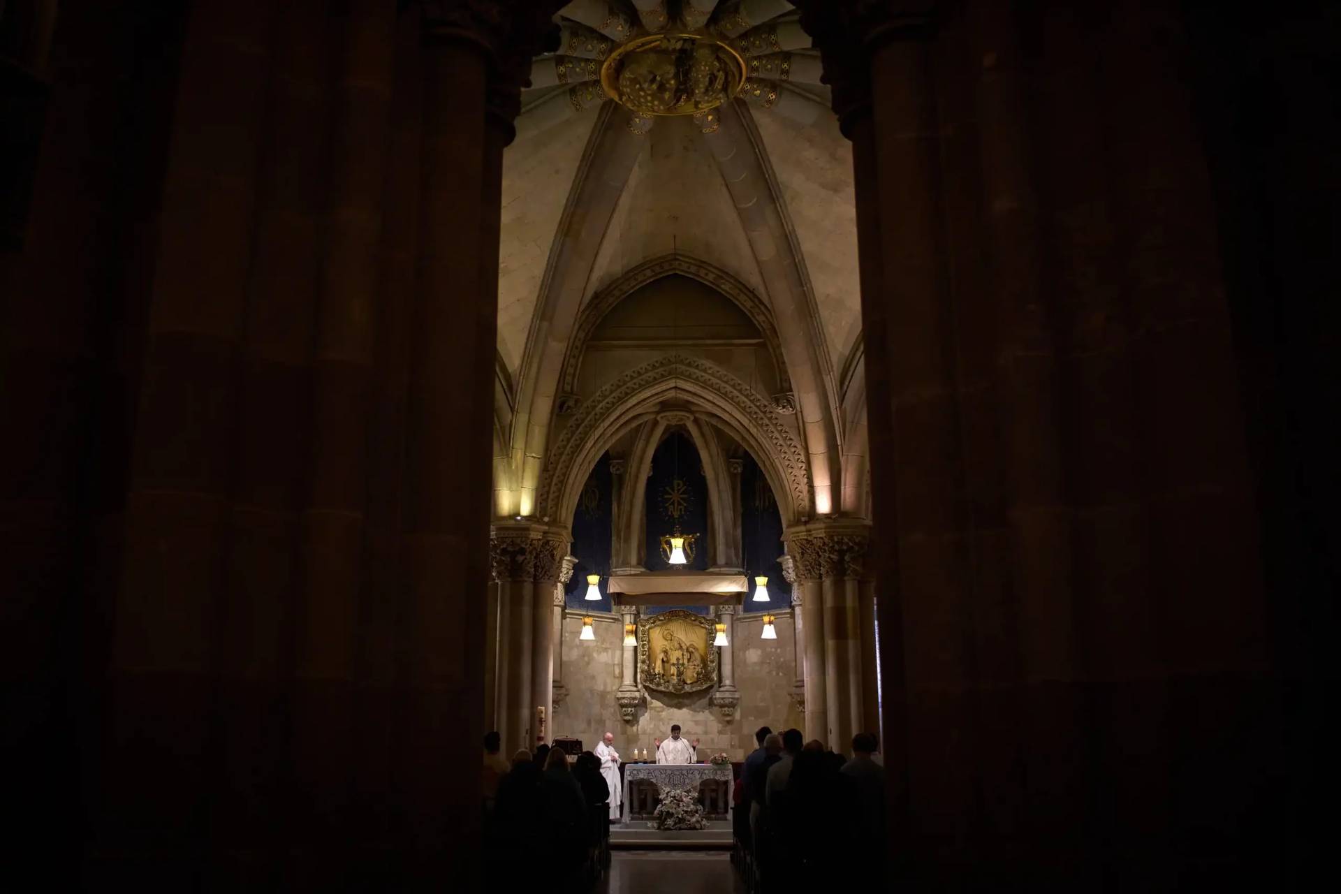 A priest celebrates Mass in the crypt of Antoni Gaudí beneath the Sagrada Familia while crowds of visitors fill the basilica above in Barcelona, Spain, May 15, 2026. (Credit: Emilio Morenatti/AP.)