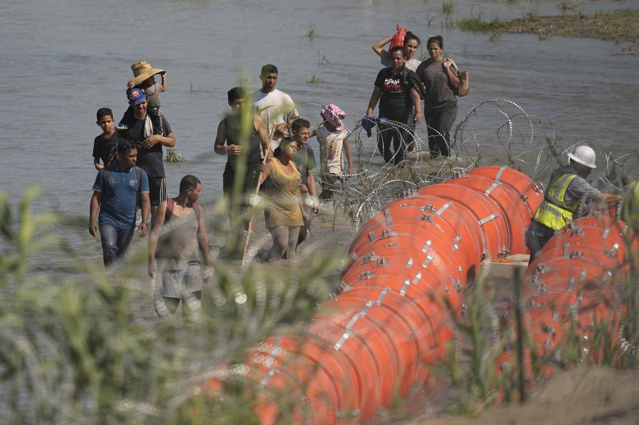 Migrants trying to enter the U.S. from Mexico approach the site where workers are assembling large buoys to be used as a border barrier along the banks of the Rio Grande in Eagle Pass, Texas, Tuesday, July 11, 2023. (Credit: Eric Gay/AP.)