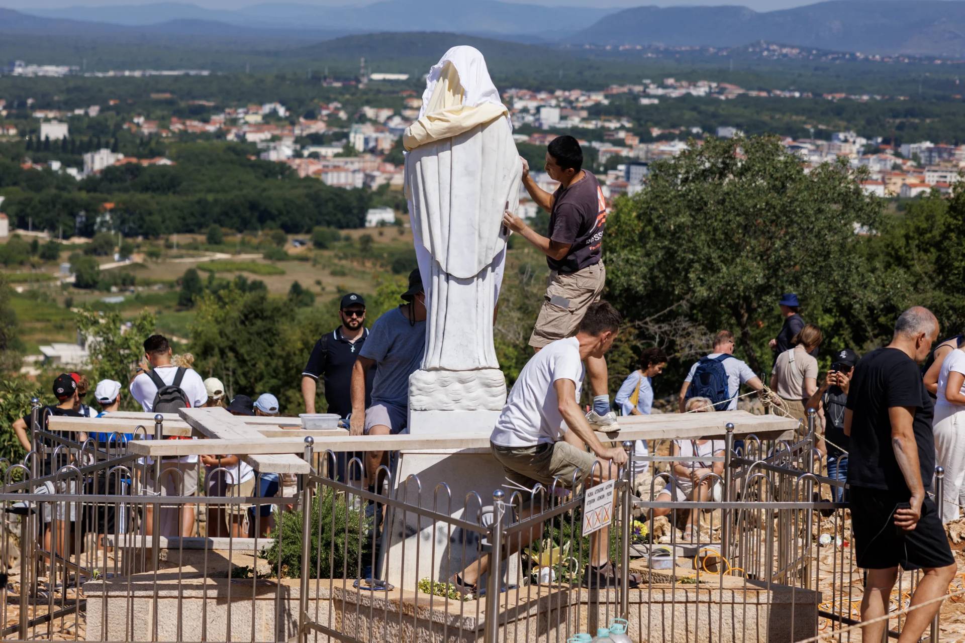 Volunteers clean the vandalized statue of the Virgin Mary, which has been covered with a white sheet, on Apparition Hill in Medjugorje, Bosnia, Tuesday, July 28, 2026. (Credit: AP Photo/AP.)