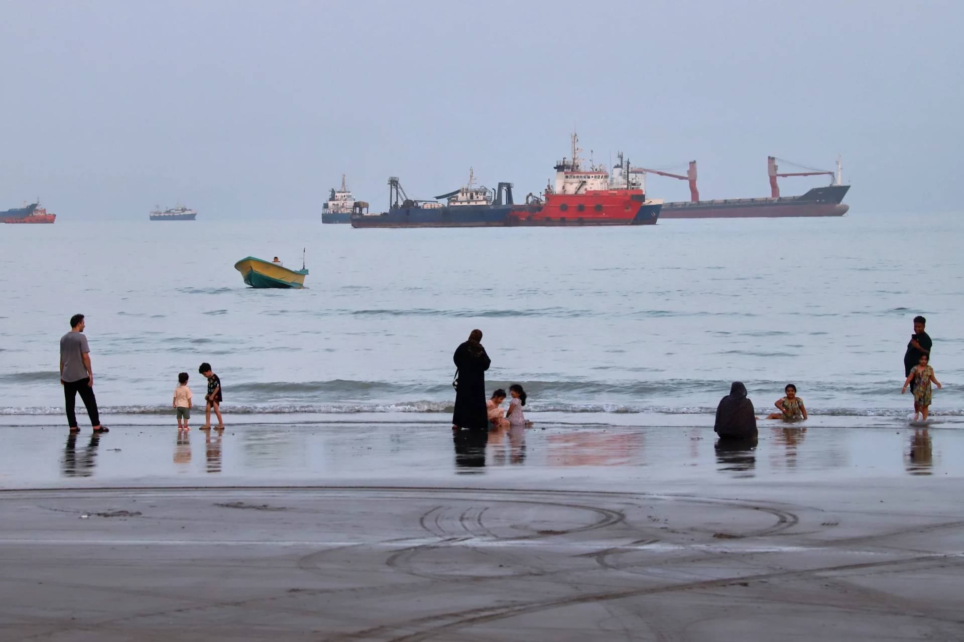 People spend time at a beach as commercial vessels are anchored in the Strait of Hormuz off Bandar Abbas, Iran, Wednesday, Aug. 5, 2026. (Credit: Amirhosein Khorgooi/ISNA via AP.)