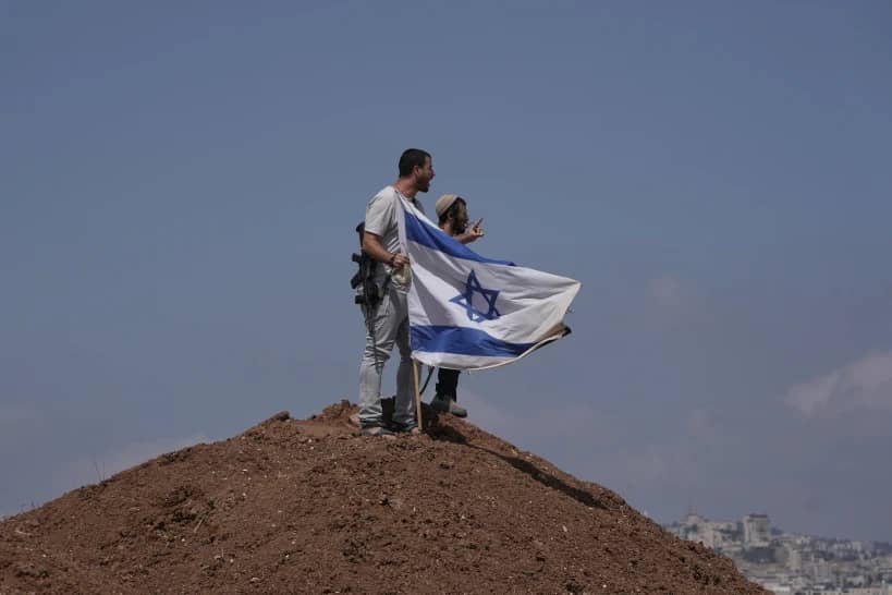 Israeli settlers put up an Israeli flag on a hilltop after it was taken down by Israeli and foreign peace activists during a protest in support of local landowners whose property is threatened with seizure by settlers, on the outskirts of the West Bank city of Beit Sahour, Friday, Aug. 14, 2026. (Credit: Mahmoud Illean/AP.)