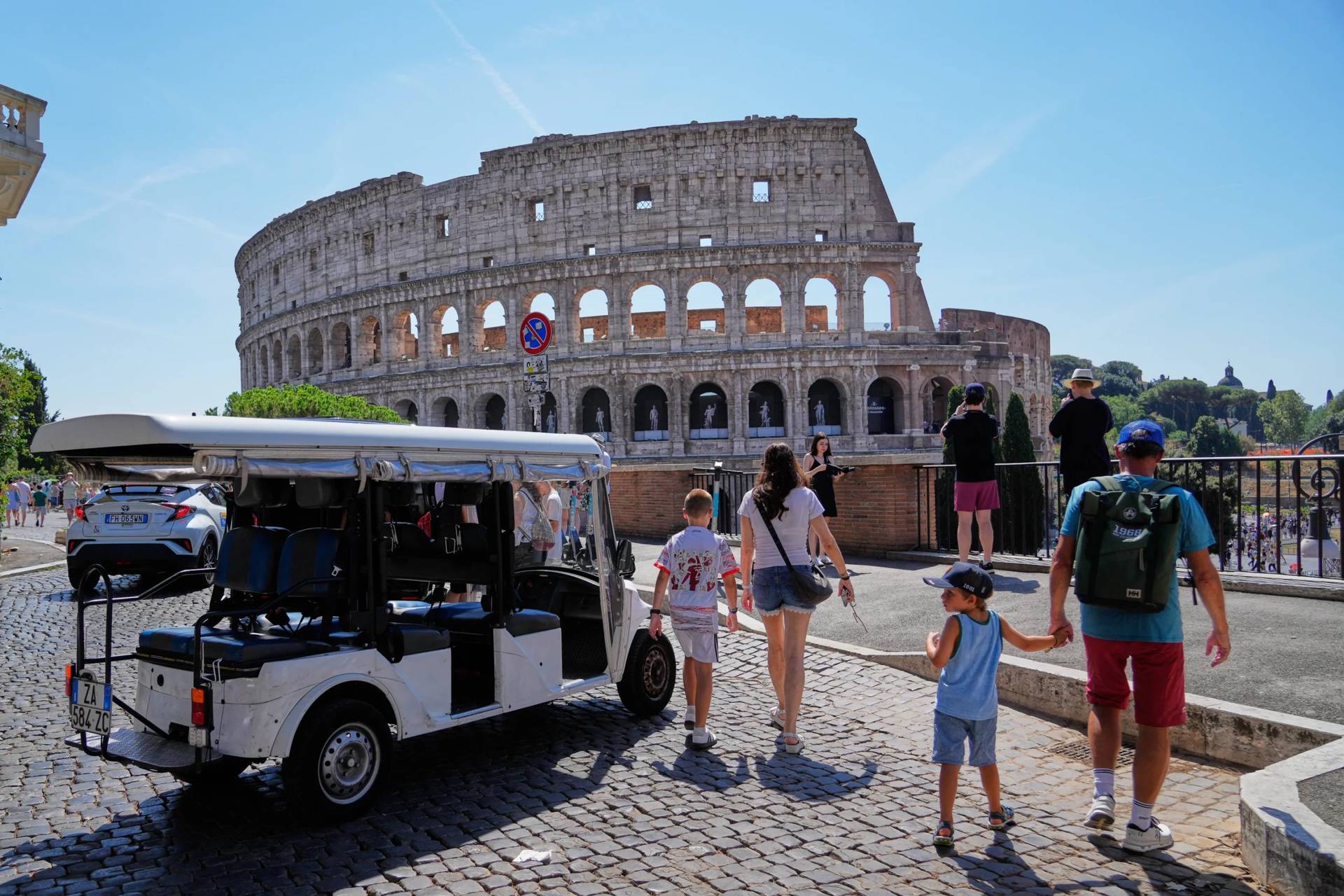 A golf cart sits near the Colosseum as tourists crowd the surrounding streets in Rome, Tuesday, Aug. 18, 2026, highlighting the growing presence of the vehicles in the capital’s historic center as authorities move to curb an industry blamed by critics for worsening congestion, illegal parking, and overtourism. (Credit: Gregorio Borgia/AP.)
