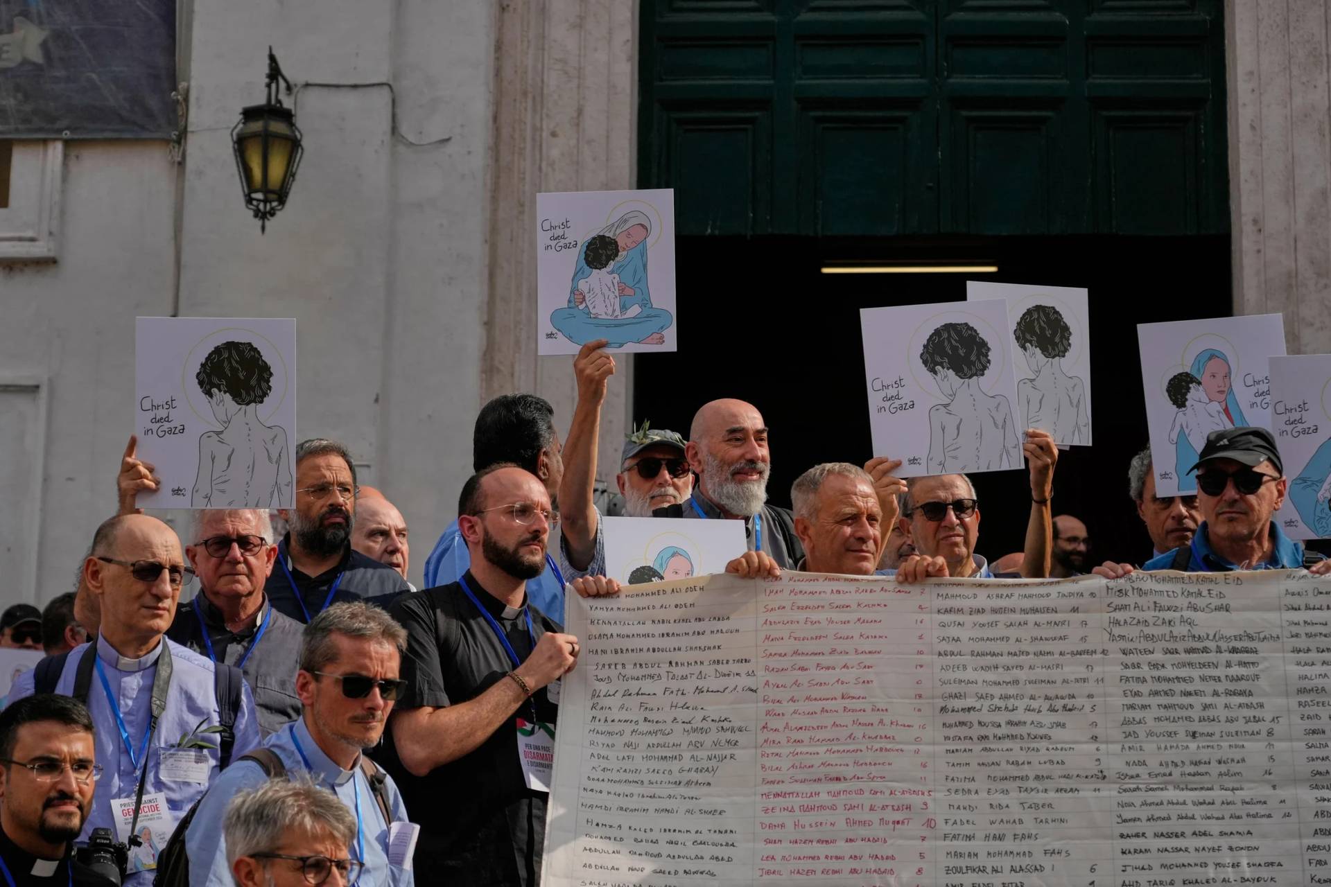 Priests from various countries, members of the "Priests Against Genocide" network, carry a shroud bearing the names of 300 Palestinian and Lebanese children whom organizers say were killed by the Israeli military after ceasefires were declared, during a demonstration near St. Peter's Square at the Vatican, Tuesday, Sept. 22, 2026. (Credit: Gregorio Borgia/AP.)