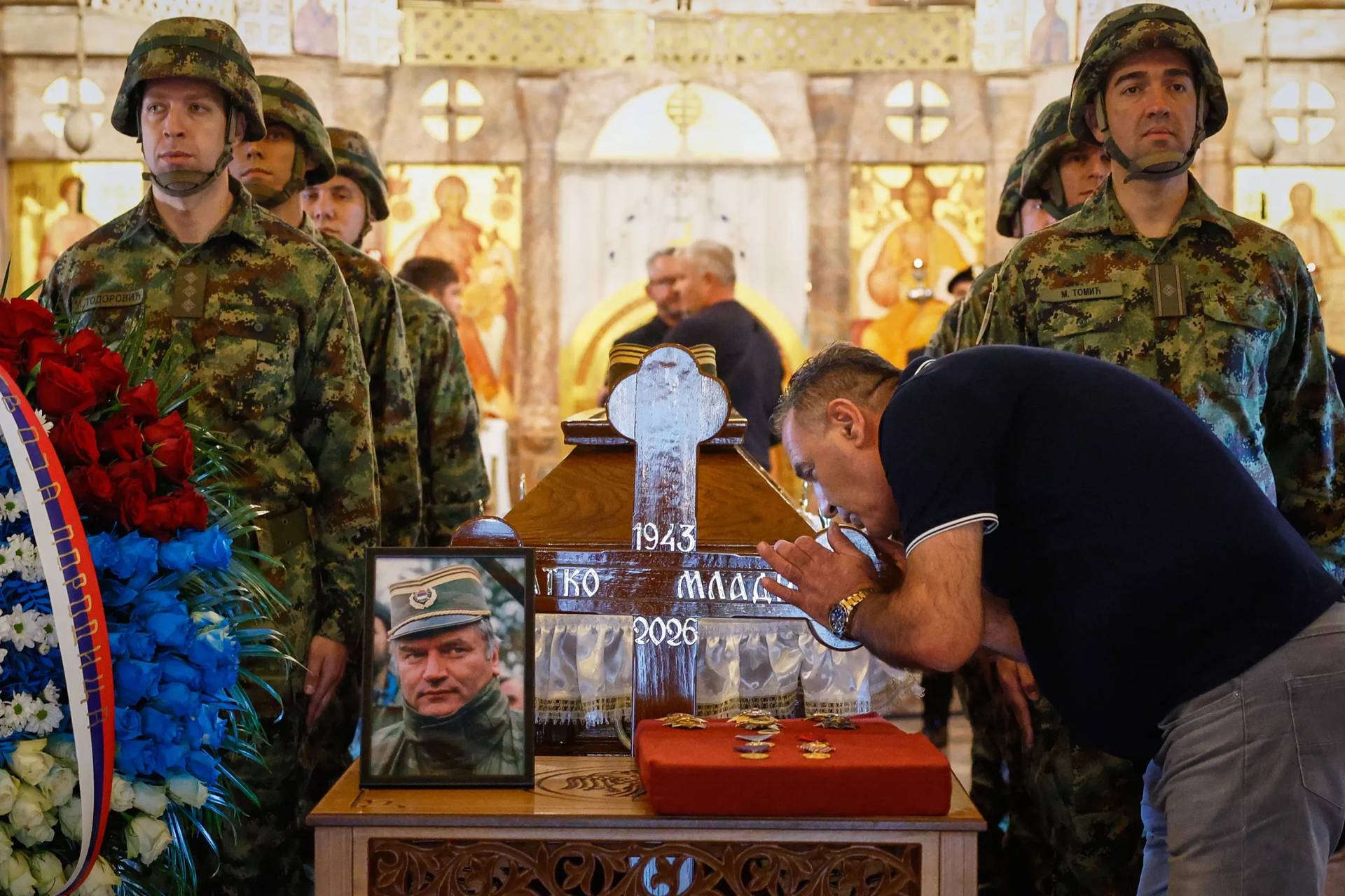 A man touches the cross as Serbian national military servicemen stand around the coffin of the former Bosnian Serb army commander Ratko Mladic, who died last week while serving a life sentence for genocide and other atrocities during the war in Bosnia, at the St. Luka Church, in Belgrade, Serbia, Monday, Sept. 7, 2026. (Credit: Marko Drobnjakovic/AP.)