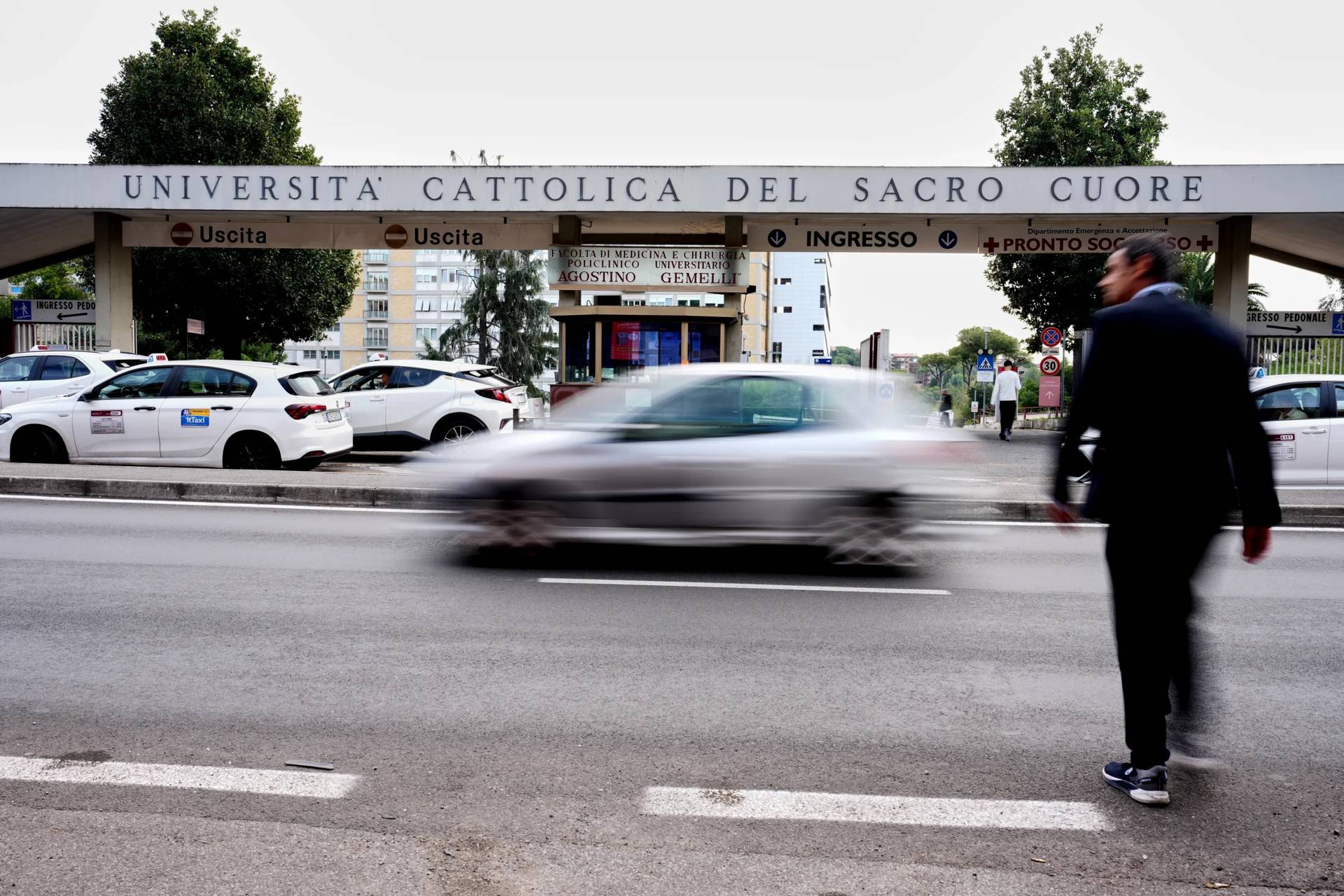 People walk past the main entrance of the Agostino Gemelli Polyclinic where Pope Leo XIV is scheduled to be hospitalized in the next days to remove a lung nodule, in Rome, Monday, Oct. 12, 2026. (Credit: Andrew Medichini/AP.)