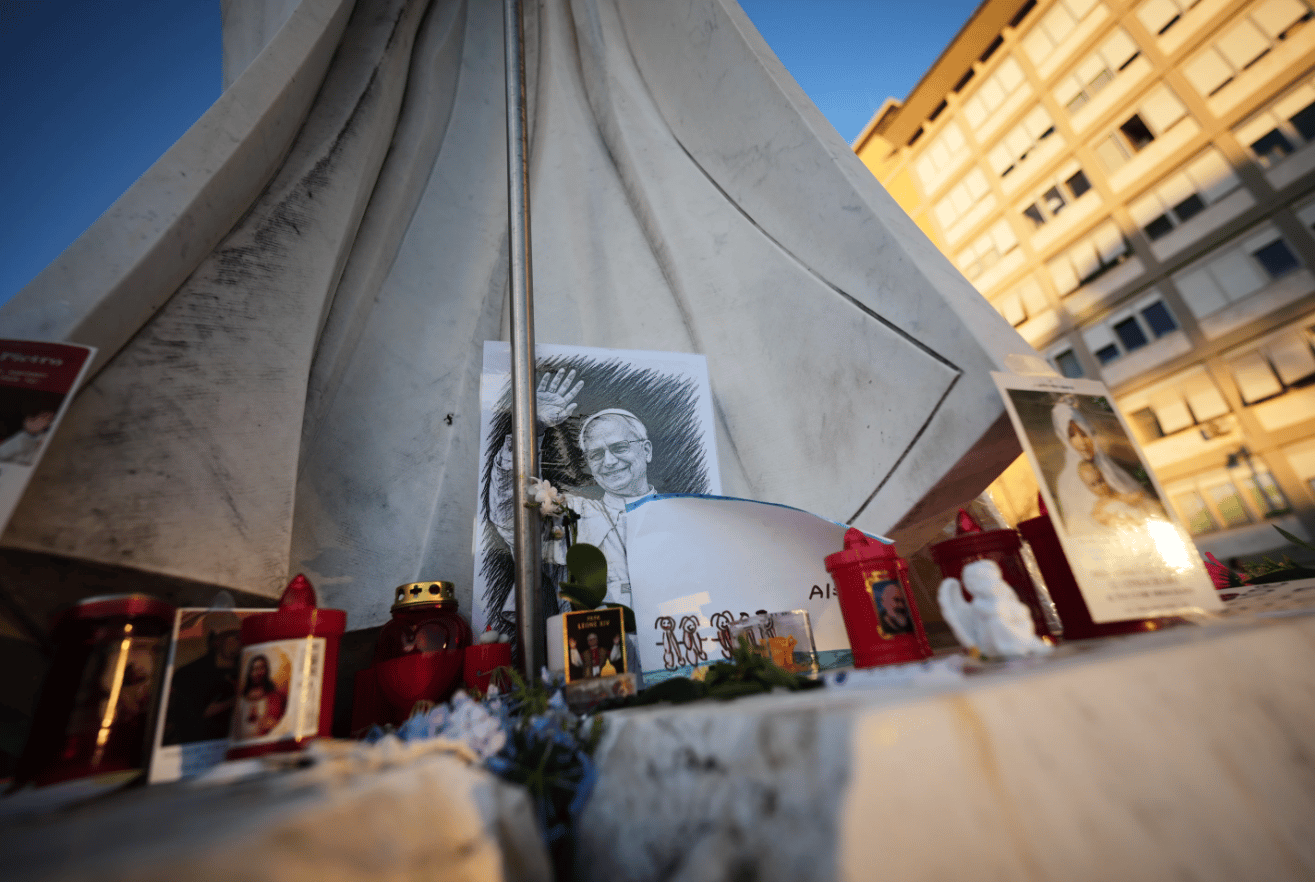 An image of Pope Leo XIV rests at the base of a statue of Pope St. John Paul II at the Agostino Gemelli Polyclinic, where Leo is hospitalized, in Rome, Friday, Oct. 16, 2026. (Credit: Andrew Medichini/AP.)