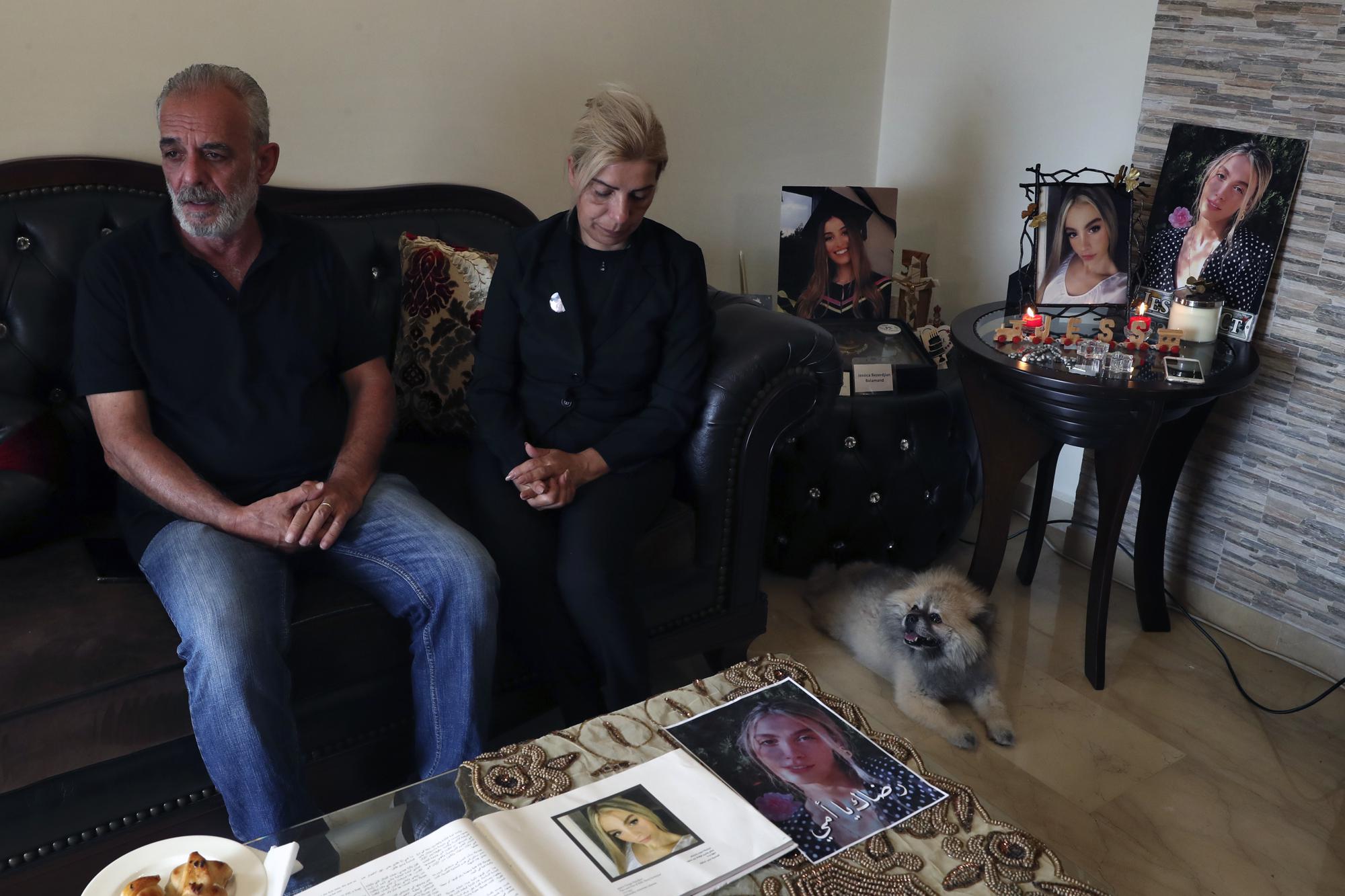 George Bezdjian and Chouchan Yeghiyan, the parents of Jessica Bezdjian, who was killed in last year's massive blast at Beirut's seaport, speak as they sit next to her pet dog Foxy and pictures of her, in Antelias, Lebanon, Monday, July 12, 2021. Bezdjian was one of four female nurses who lost their lives at the Saint George Hospital University Medical Center that day, including her close friend Jessica Kahwaji who was instantly killed. (AP Photo/Bilal Hussein)
