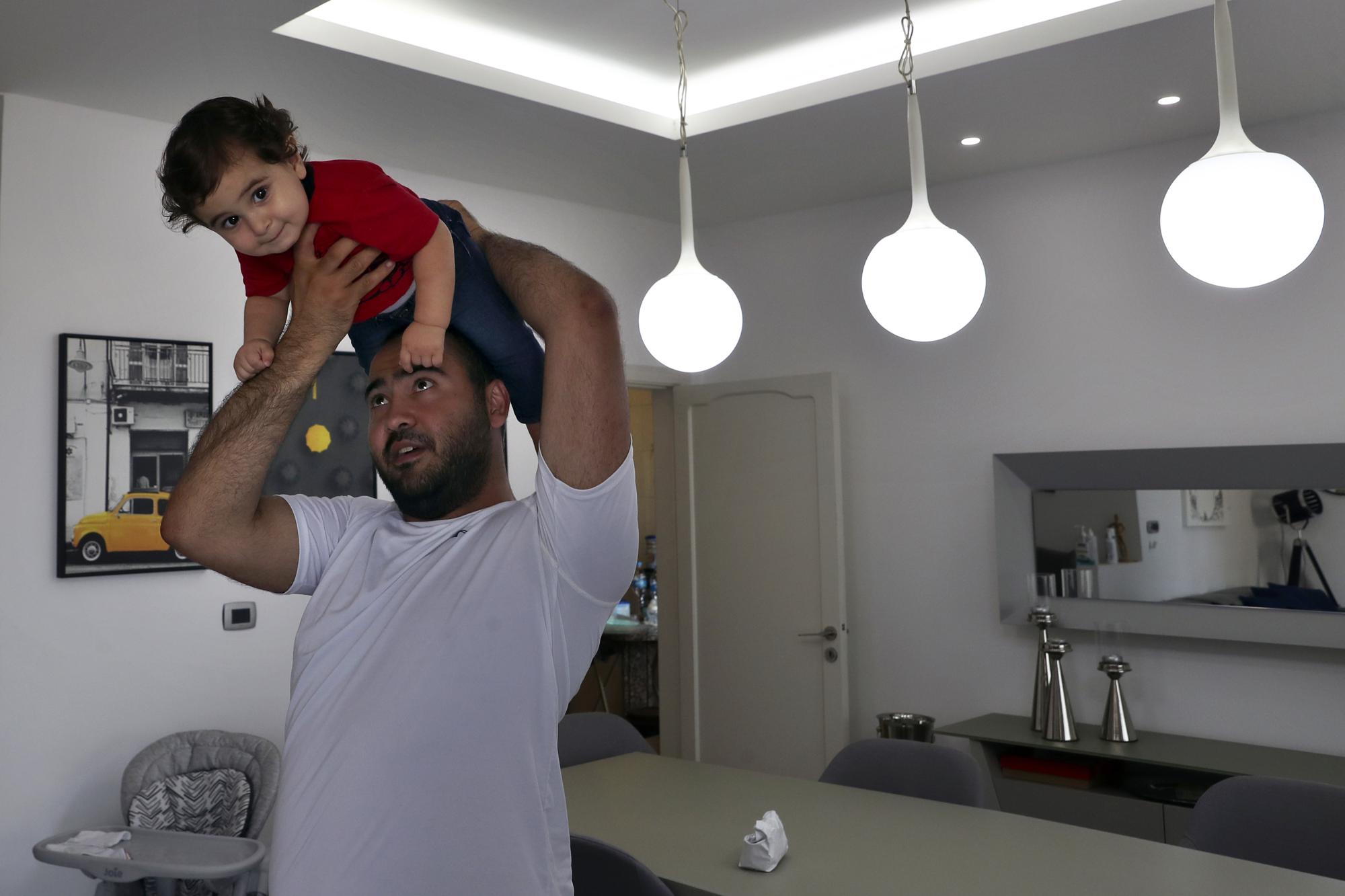 Edmond Khnaisser holds up his son, one-year-old Georges, at his house in the town of Jal el-Dib, north of Beirut, Lebanon, Tuesday, July 10, 2021. Khnaisser's wife, Emmanuelle, was about to give birth to her first son and was in the last stages of labor when the massive blast tore through the hospital, smashing windows, doors and machines in the operations room and riddling her lower body with tiny pieces of flying glass. (AP Photo/Bilal Hussein)